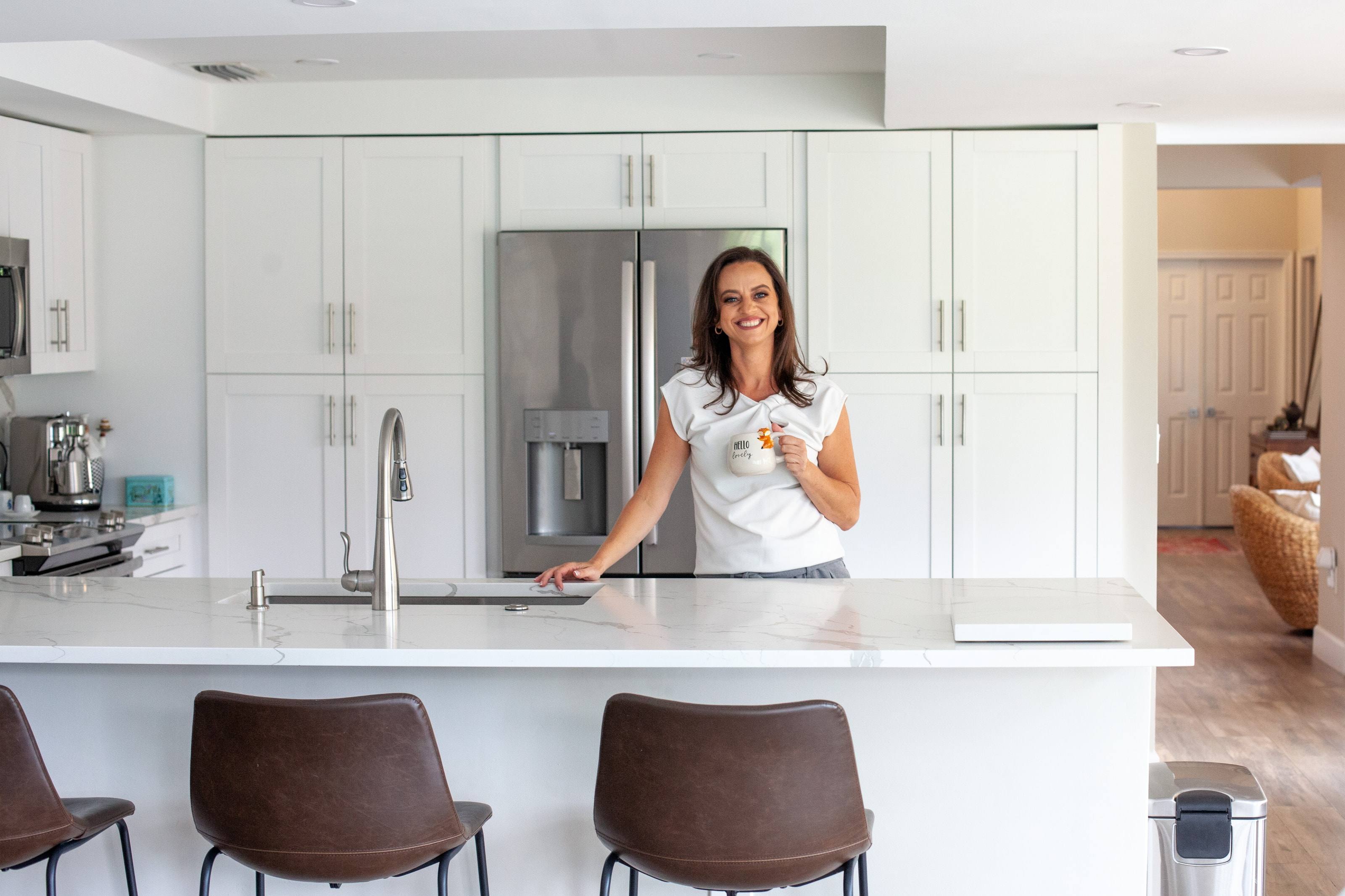 Anaie Amorim sonriendo en la isla de una cocina, con una taza de café